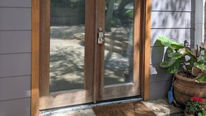 A wooden double door with a glass panel, a doormat, a potted plant, and a wall-mounted light fixture.