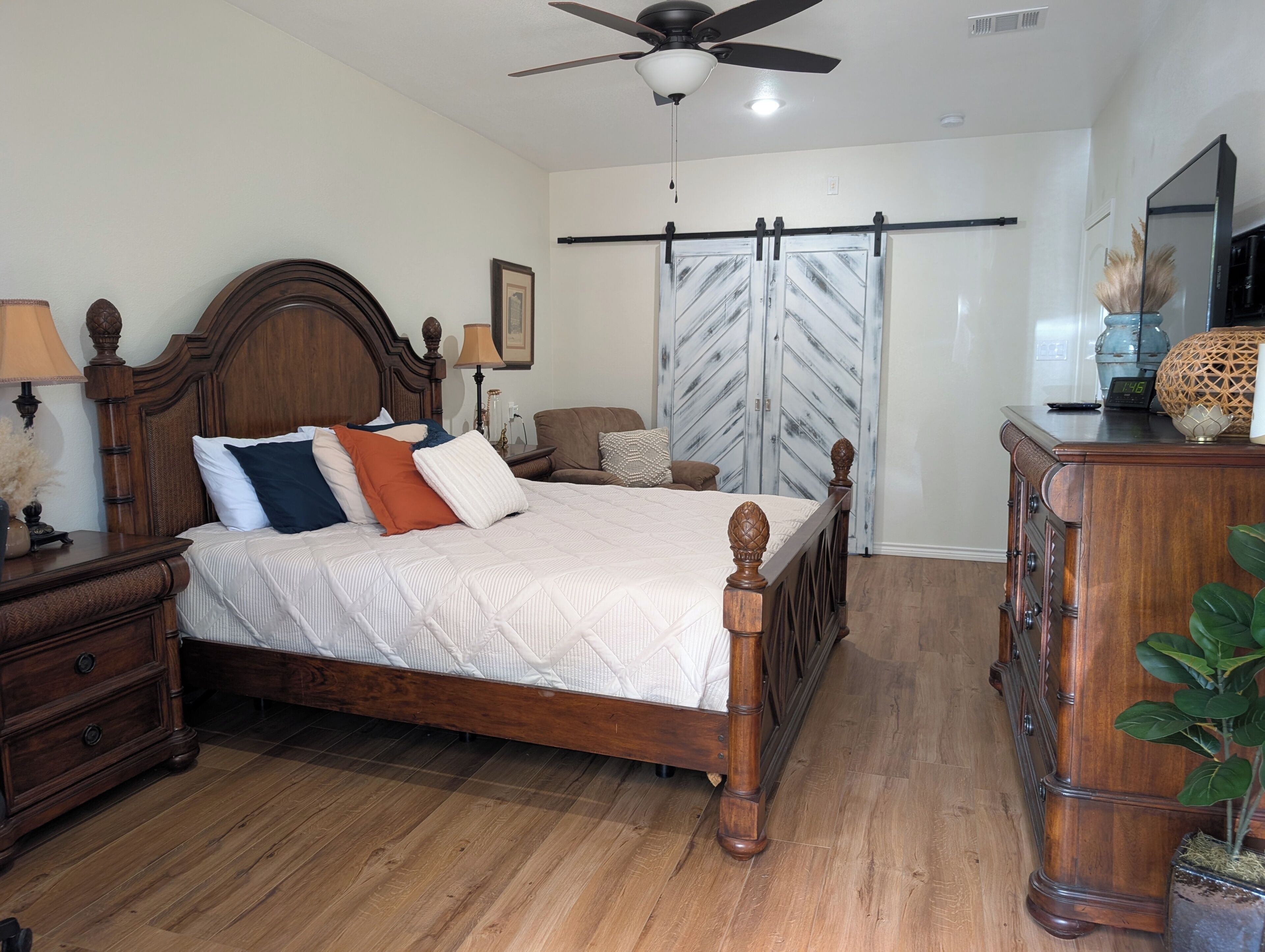 A bedroom with a wooden bed, a nightstand, a dresser, a ceiling fan, and a large window with a view.