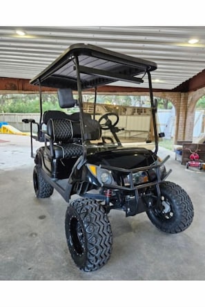 A black golf cart with large tires and a canopy, parked inside a covered garage.