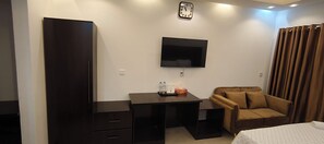 Una habitación de hotel con escritorio, una silla, una cama, un televisor y un reloj en la pared.