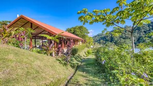 A house with a red roof, surrounded by lush greenery and a clear view of a lake. - Villa 9B Toucan Valley Jungle Village Resort (Ciudad Cortés)