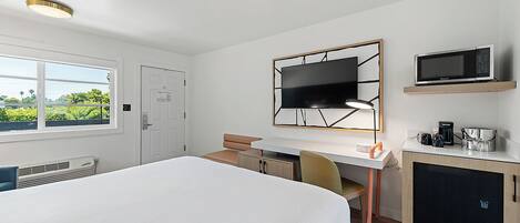 A hotel room with a bed, a desk, a chair, a TV, and a coffee maker.