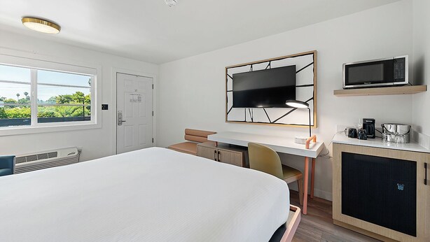 A hotel room with a bed, a desk, a chair, a TV, and a coffee maker.
