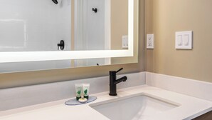A bathroom with a white sink, a large mirror, a black faucet, and two green spa products on the counter.
