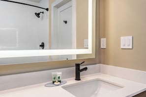 Un baño con un lavabo blanco, un espejo grande, un grifo negro y dos productos de spa verdes sobre la encimera.