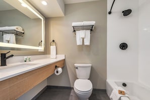 Ein modernes Badezimmer mit Waschbecken, Toilette und Badewanne in Weiß. Handtuchhalter mit Handtüchern und Toilettenpapierhalter sind vorhanden.
