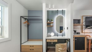 A compact bedroom with a bed, bedside table, mirror, and a small seating area.