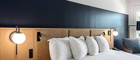 A hotel room with a bed, bedside lamps, a nightstand, and a chair.