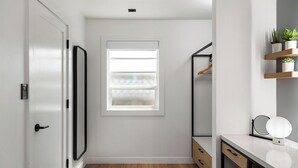 A narrow hallway with a window, a door, a mirror, and a small shelf with plants.