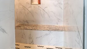 A bathroom with marble walls, a built-in shelf, and a patterned floor.