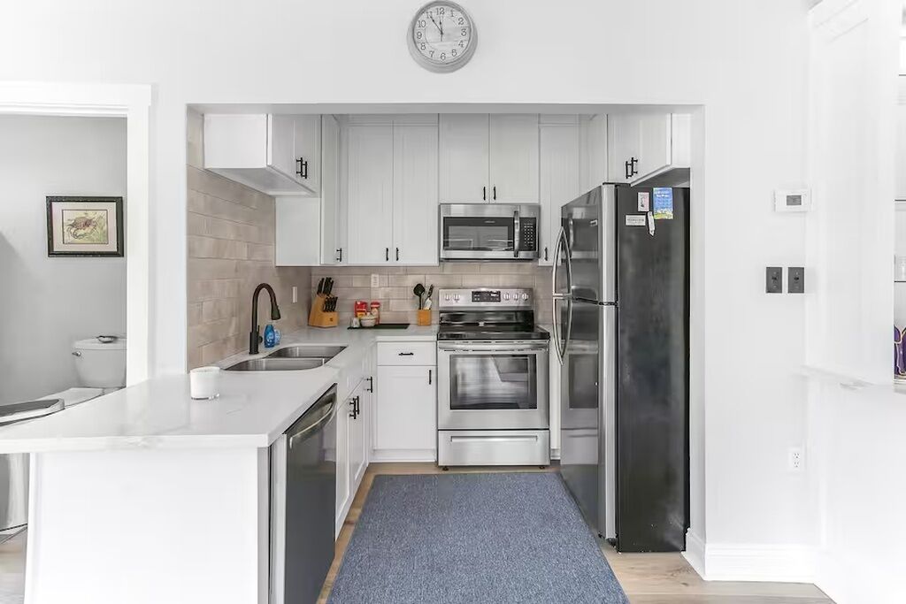 Eine moderne Küche mit weißen Schränken, Edelstahlgeräten, einer Mikrowelle, einem Backofen und einem Kühlschrank.
