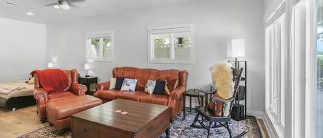 A spacious living room with a large window, a ceiling fan, and a patterned rug.
