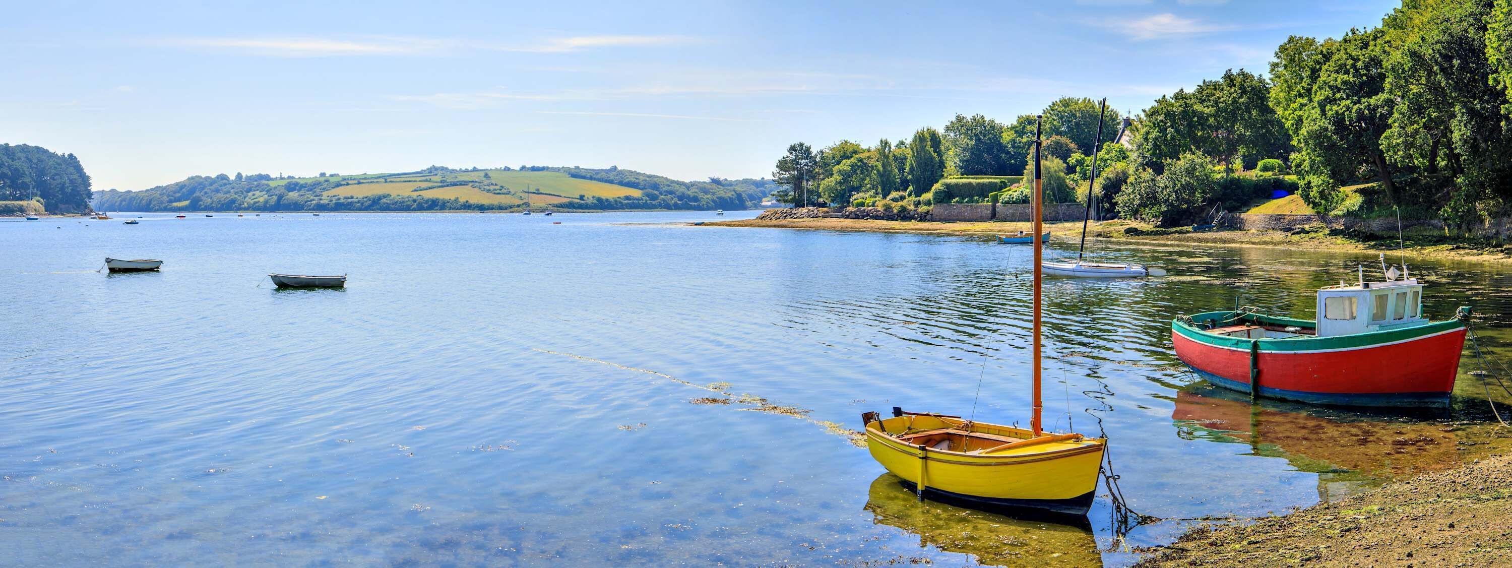 Ein ruhiger See mit Booten, einem klaren Himmel und einer hügeligen Landschaft im Hintergrund.