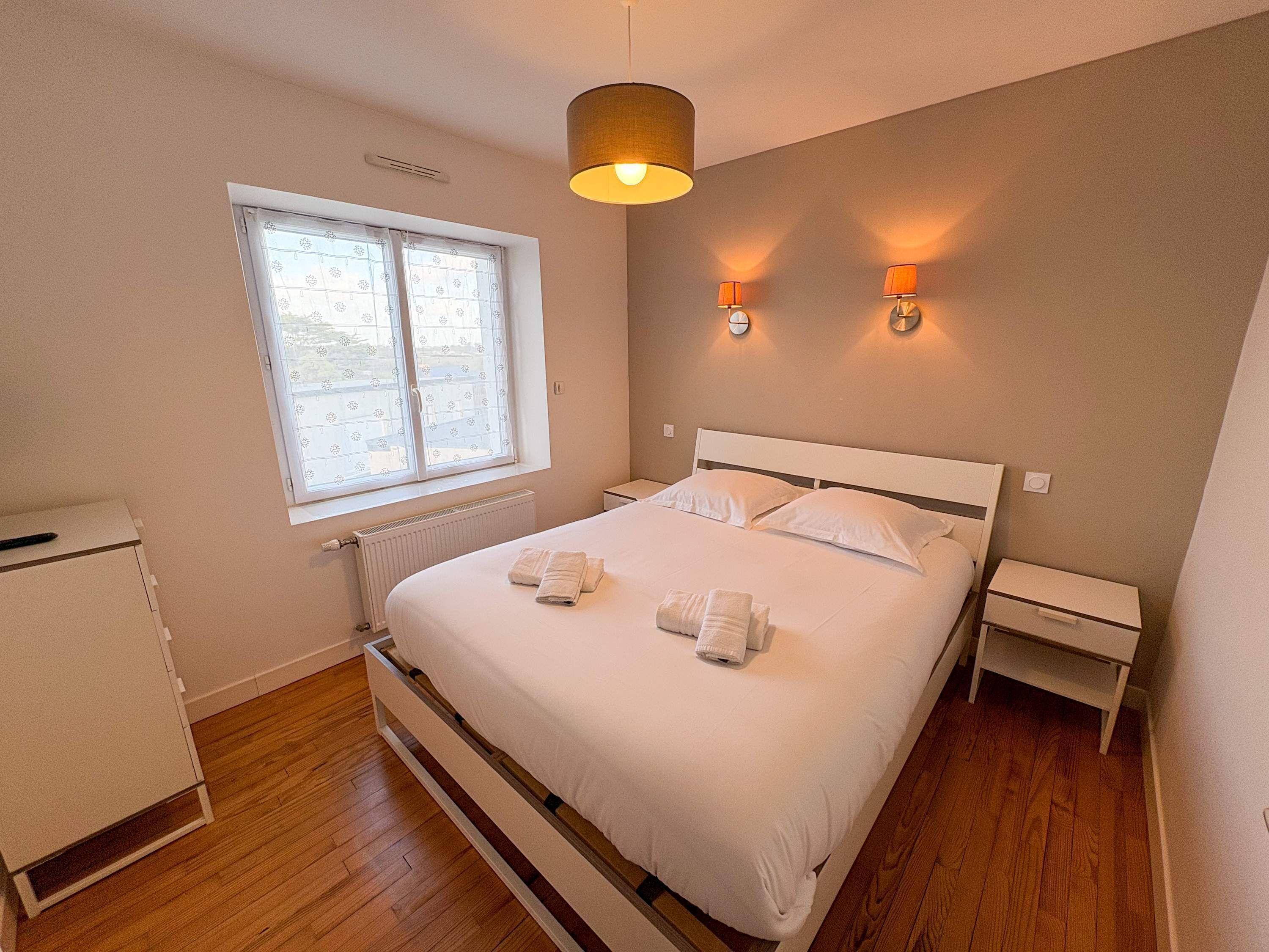 Een slaapkamer met een bed, twee nachtkastjes, een raam en een radiator.