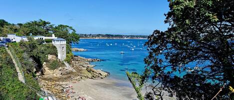 Vista costera con playa, costa rocosa y embarcaciones en el agua.