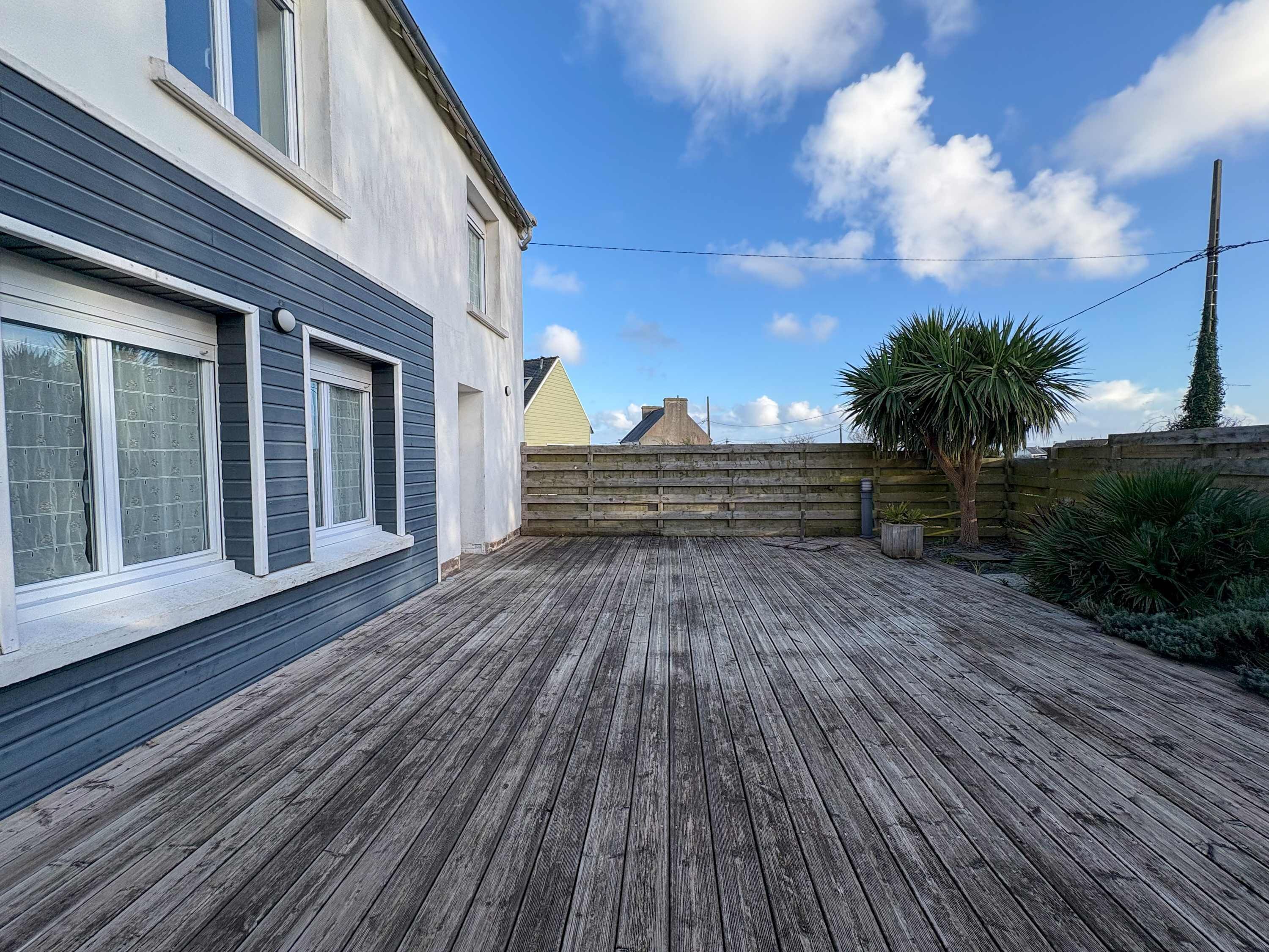 Una terraza de madera con una casa al fondo.