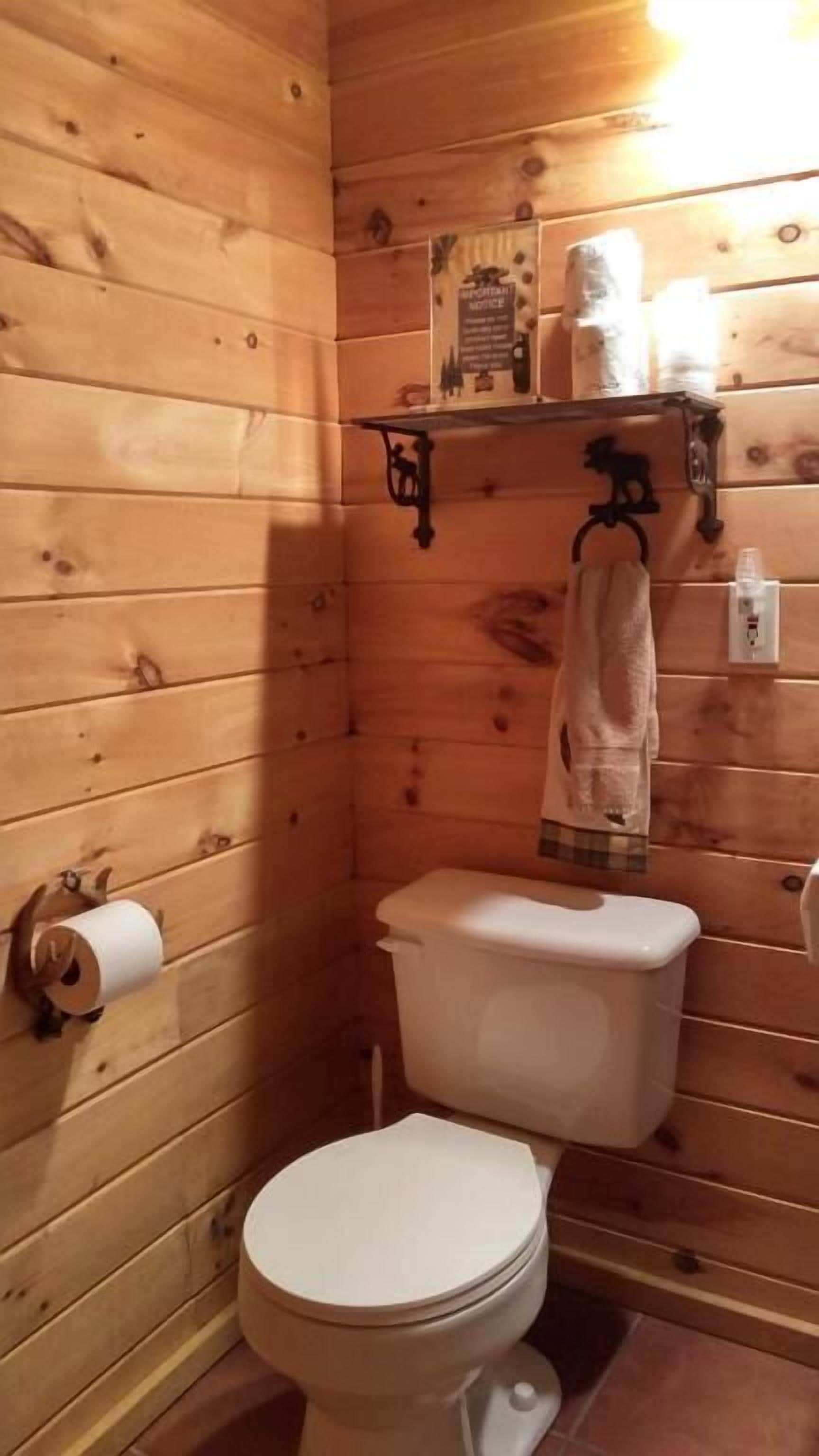 Une salle de bain aux murs lambrissés, avec des toilettes, une serviette accrochée au mur et une étagère contenant des articles de toilette.