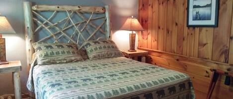 A bed with a patterned bedspread, a wooden headboard, two bedside lamps, and a framed picture on the wall.