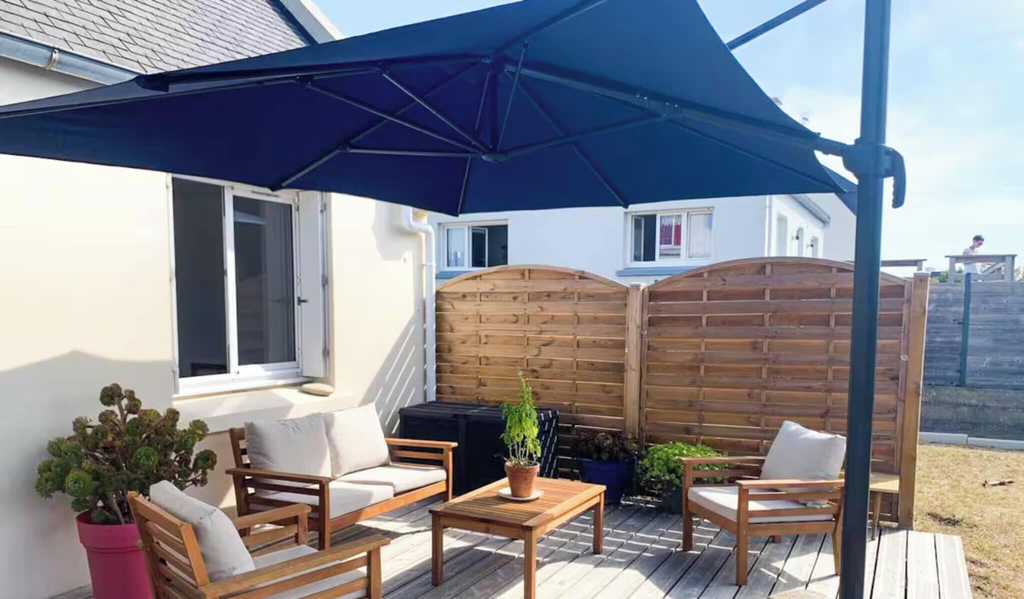 Eine Terrasse mit Holzmöbeln, einem großen Sonnenschirm und einem Holzzaun.