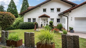 Een huis met twee verdiepingen, een witte gevel, een dak van rode tegels en een voordeur met een klein portaaltje.