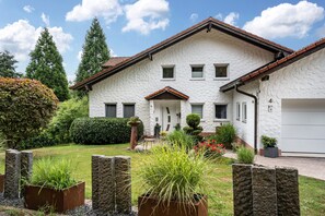 A two-story house with a white exterior, a red-tiled roof, and a front door with a small porch. - Apartment 'Ferienglück Vogelsang' with Private Terrace, Garden, and Wi-Fi (Loßburg)