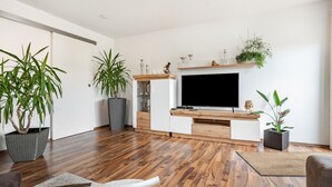 Een moderne woonkamer met een flatscreen televisie, houten vloer en potplanten.