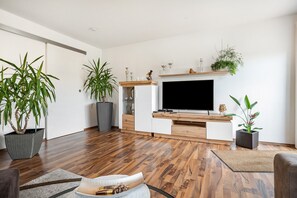 A modern living room with a flat-screen TV, wooden flooring, and potted plants. - Apartment 'Ferienglück Vogelsang' with Private Terrace, Garden, and Wi-Fi (Loßburg)