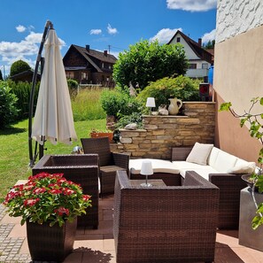 An outdoor patio with wicker furniture, a stone wall, and a white umbrella. - Apartment 'Ferienglück Vogelsang' with Private Terrace, Garden, and Wi-Fi (Loßburg)