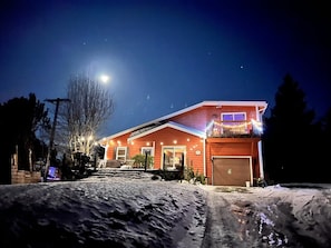 Una casa de dos pisos con garaje, un balcón con luces y una entrada cubierta de nieve.