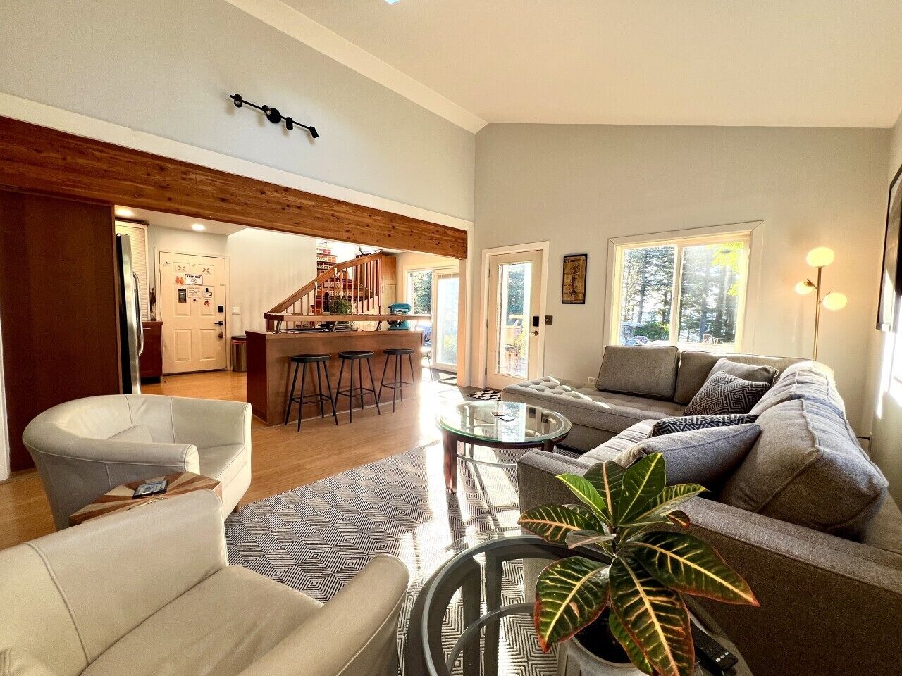 A modern living room with a sofa, armchairs, a coffee table, and a dining area with bar stools.