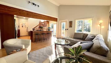A modern living room with a sofa, armchairs, a coffee table, and a dining area with bar stools.