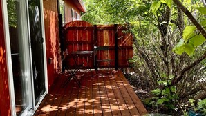 A wooden deck with a glass table and chairs, surrounded by a red fence and greenery. - THE HIDE AWAY | 1 Bedroom King Suite (Kodiak)