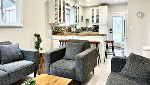 A modern living room with grey sofas, a wooden coffee table, and a kitchen in the background. - THE HIDE AWAY | 1 Bedroom King Suite (Kodiak)