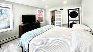 A bedroom with a bed, a TV, a wardrobe, a washing machine, and a window. - THE HIDE AWAY | 1 Bedroom King Suite (Kodiak)