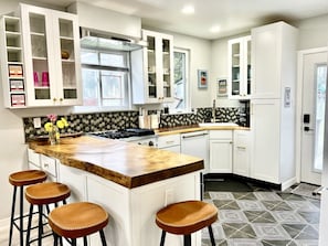 A kitchen with white cabinets, a wooden island with stools, a patterned backsplash, and a black and white tiled floor.
