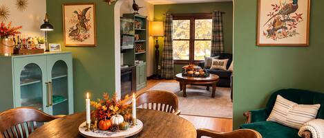 A dining area with a round wooden table, chairs, and a centerpiece with candles and pumpkins.