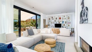Una sala de estar moderna con un sofá modular, un televisor de pantalla plana y una estantería llena de objetos decorativos.