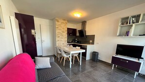 A modern living room with a grey sofa, a dining table with chairs, a kitchen area with a TV, and a bookshelf. - «Mon Havre» 6p centre ville au calme, wifi (Quiberon)