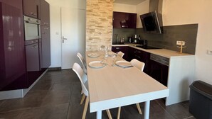 A compact kitchen with a dining area, including a table set for two, a built-in oven, and a stone accent wall. - «Mon Havre» 6p centre ville au calme, wifi (Quiberon)