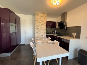 Une cuisine compacte avec un coin repas, comprenant une table pour deux personnes, un four encastré et un mur décoratif en pierre.