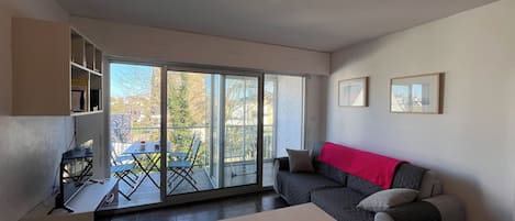 En moderne stue med sofa, spisebord med vinglas, balkon med bord og stole, samt en skydedør til terrassen.