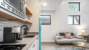 Een moderne keuken met een koffiezetapparaat, een blauwgroene koelkast, en een zithoek met een bank en een lamp.
