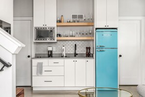 Eine moderne Küche mit weißen Schränken, einem blauen Kühlschrank, einer Mikrowelle und einer Küchenwand mit Backsteinoptik.