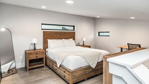 Een moderne slaapkamer met een houten bed, nachtkastjes, een bureau en een spiegel.
