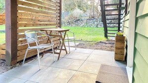 A patio with a table and chairs, a wooden fence, and a garden view. - Skovhaven West Coast Suite in Upper Gibsons, minutes away from the beach & more! (Gibsons)