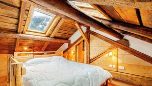 Interior de una cabaña de madera con cama, tragaluz y vigas de madera.