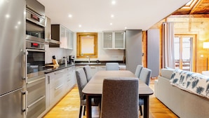 Una cocina moderna con electrodomésticos de acero inoxidable, un comedor con sillas tapizadas en gris y suelo de madera.