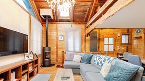 Un acogedor interior de cabaña con piso de madera, un sofá gris, una mesa de centro de madera, un televisor y una chimenea.