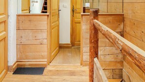 Interior de madera con una escalera, una puerta que da a otra habitación y un pequeño banco de madera.