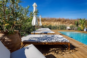 A poolside area with lounge chairs and umbrellas, a wooden deck, and a clear blue sky. - Tavirabliss Signature Villa (Tavira)